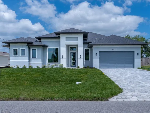 Prairie-style home with a garage, a front lawn, decorative driveway, stucco siding, and a shingled roof