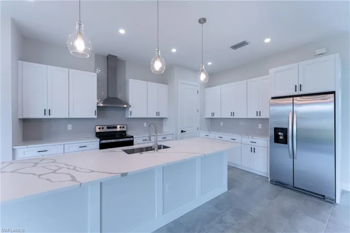 Kitchen with stainless steel appliances, tasteful backsplash, white cabinets, hanging light fixtures, and light stone countertops