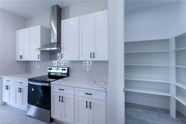 Kitchen featuring stainless steel electric range oven, white cabinetry, backsplash, and light stone countertops
