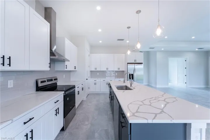 Two tone kitchen with stainless steel appliances, an island with sink, decorative backsplash, light stone countertops, and decorative light fixtures