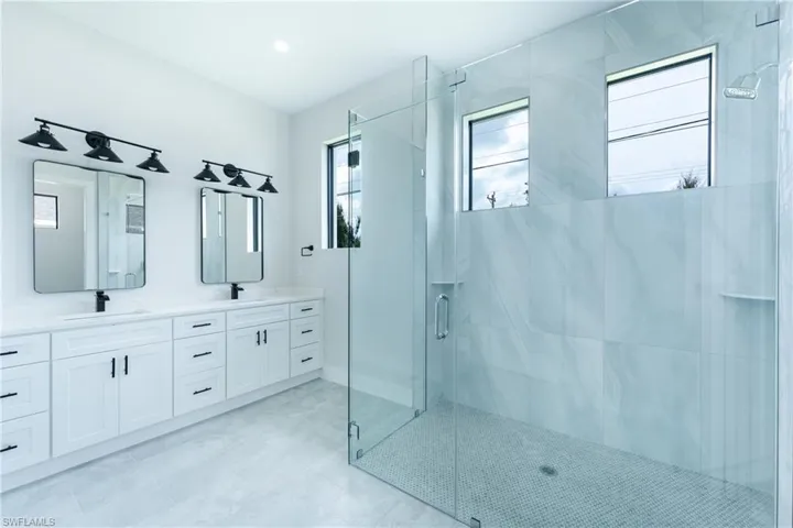 Full bath featuring double vanity and a marble finish shower