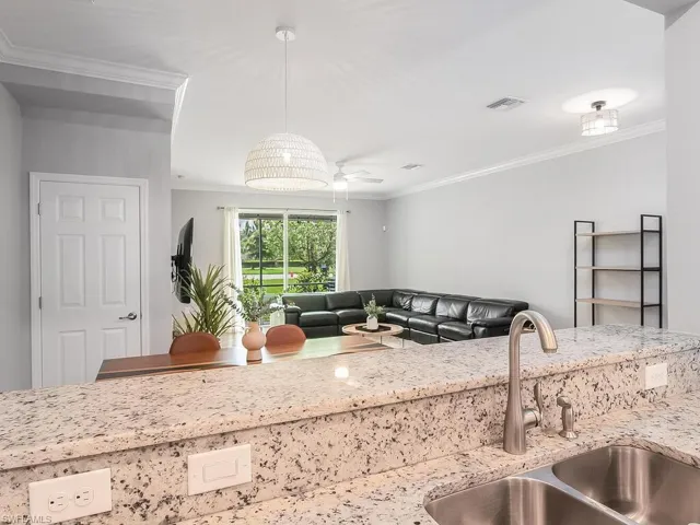 Kitchen with light stone countertops, ornamental molding, hanging light fixtures, sink, and ceiling fan