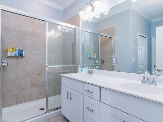 Bathroom featuring crown molding, dual sinks, a shower with shower door, and oversized vanity