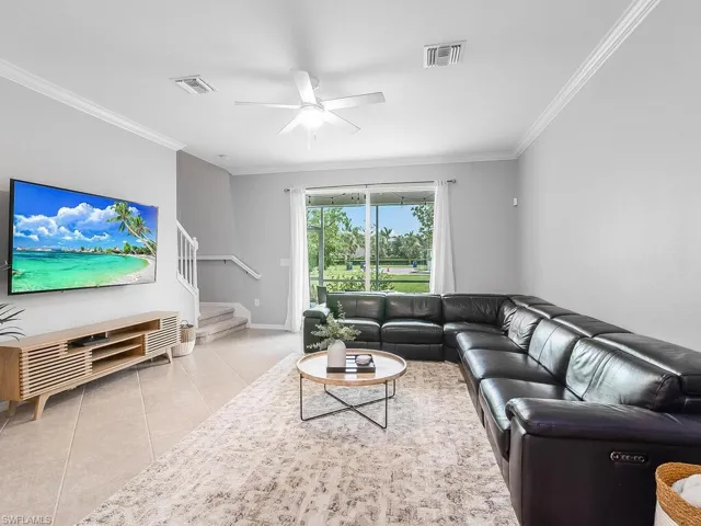 Living room with ceiling fan, crown molding, and light tile floors