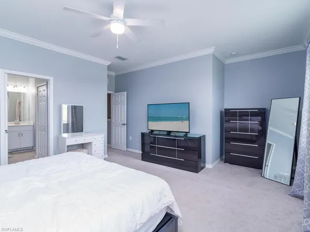 Carpeted bedroom featuring ornamental molding, ensuite bathroom, and ceiling fan