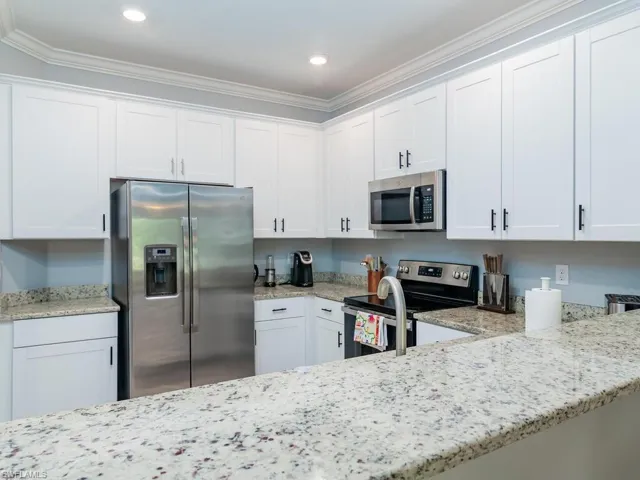 Kitchen featuring appliances with stainless steel finishes, crown molding, white cabinets, and light stone countertops