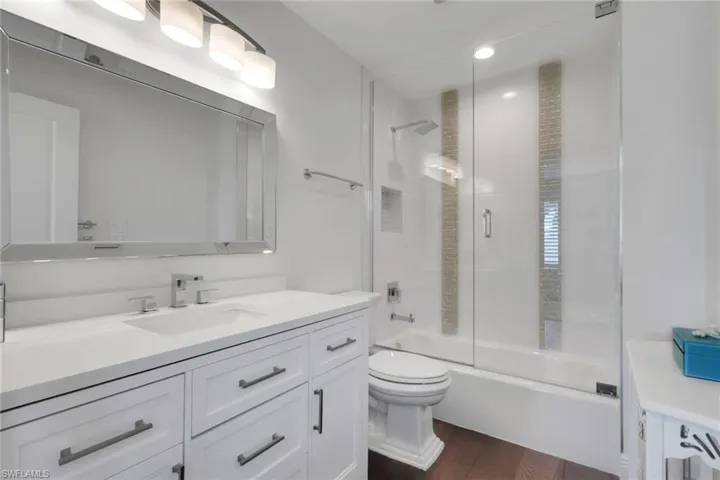 Full bathroom with vanity, bath / shower combo with glass door, and dark wood-style floors