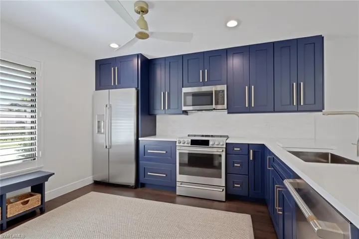 Kitchen with blue cabinetry, stainless steel appliances, light stone counters, dark wood-style floors, and recessed lighting