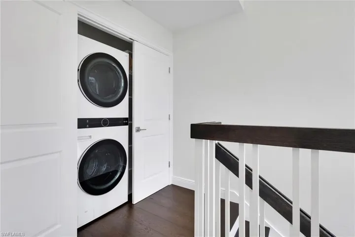 Washroom with stacked washing machine and dryer and dark wood finished floors