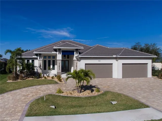 Prairie-style home featuring a tile roof, stucco siding, a front yard, decorative driveway, and a garage
