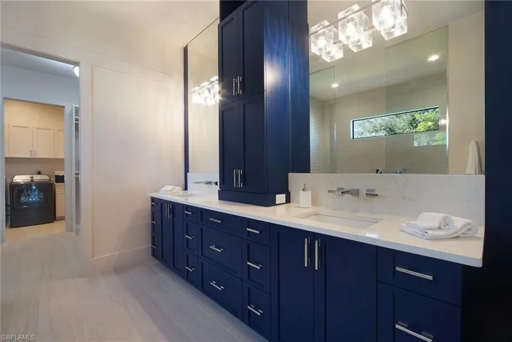 Bathroom with double vanity, washer / dryer, light wood-style flooring, and a tile shower