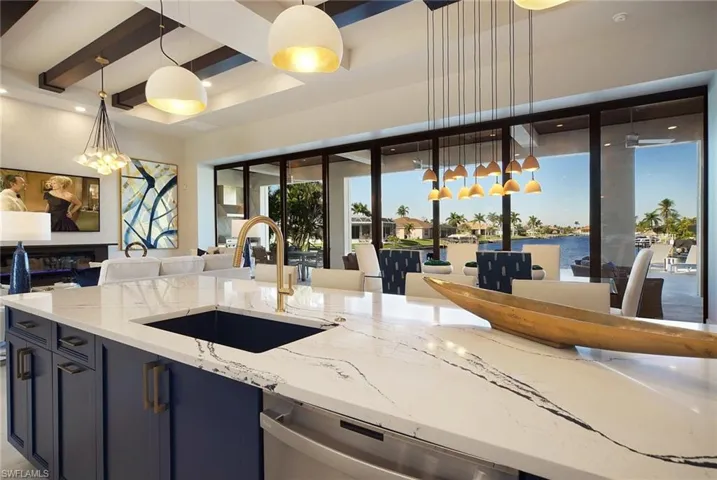 Kitchen featuring light stone countertops, blue cabinets, stainless steel dishwasher, a water view, and hanging light fixtures