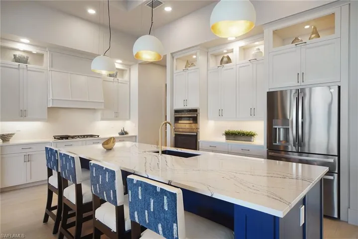 Kitchen with glass insert cabinets, appliances with stainless steel finishes, light stone counters, a kitchen bar, and recessed lighting