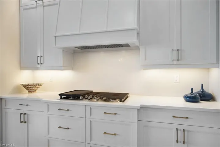 Kitchen with white cabinetry, light stone countertops, stainless steel gas stovetop, and premium range hood