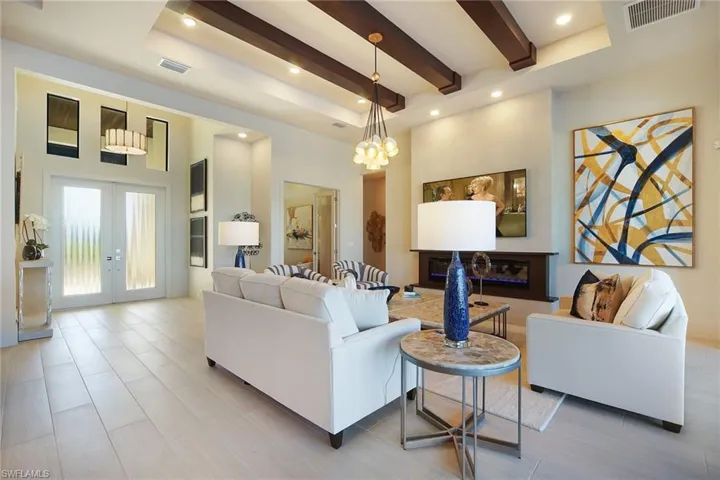 Living room featuring a glass covered fireplace, a high ceiling, beamed ceiling, french doors, and a chandelier
