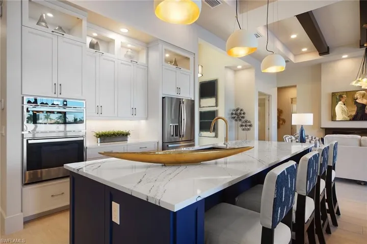 Kitchen featuring light stone counters, glass insert cabinets, pendant lighting, light wood-type flooring, and recessed lighting
