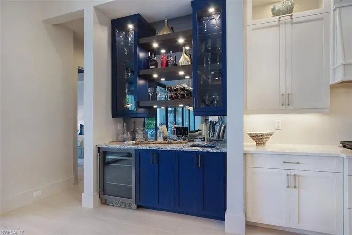 Indoor bar with glass insert cabinets, wine cooler, light stone counters, and extractor fan
