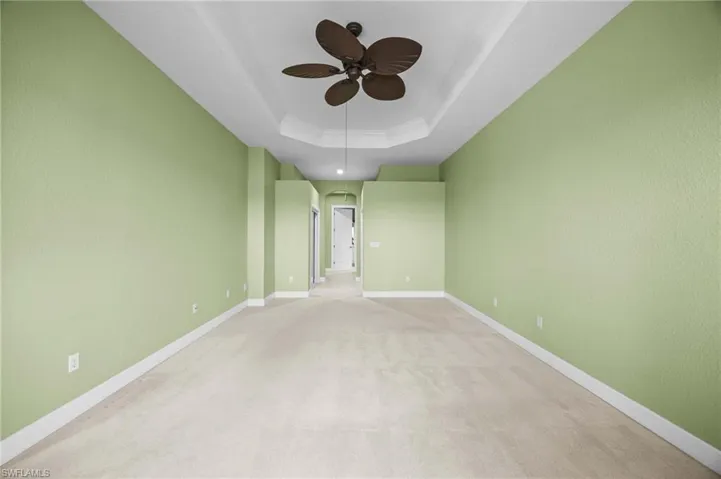 Carpeted empty room featuring ceiling fan and a tray ceiling
