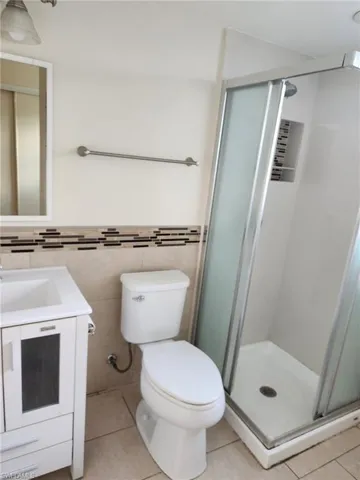Full bathroom featuring a shower stall, vanity, light tile patterned floors, tile walls, and wainscoting