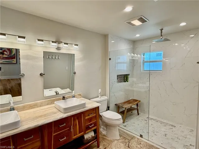 Dual vessel sinks with individual mirrors, natural wood vanity with storage, tile flooring, and a glass-enclosed shower with a rain shower head