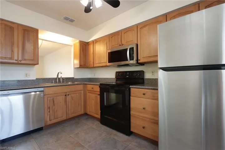 Kitchen featuring stainless steel appliances, dark countertops, a ceiling fan, and brown cabinets
