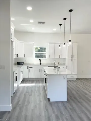 Kitchen featuring decorative light fixtures, white cabinetry, light wood-style floors, and a kitchen island