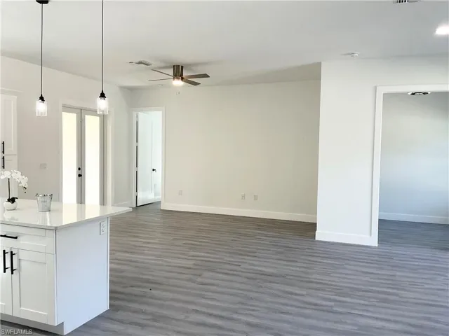 Kitchen with decorative light fixtures, open floor plan, white cabinets, light stone counters, and dark wood-style floors