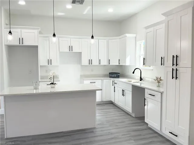 Kitchen featuring white cabinetry, pendant lighting, light stone counters, light wood-style flooring, and a center island