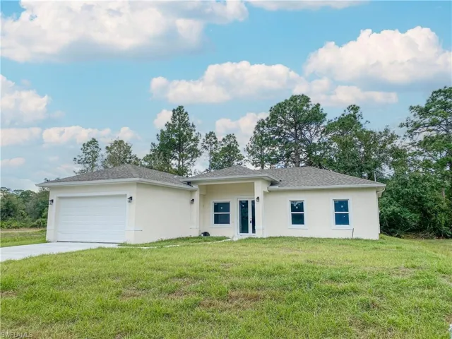 View of front of house with a front yard, stucco siding, an attached garage, and driveway