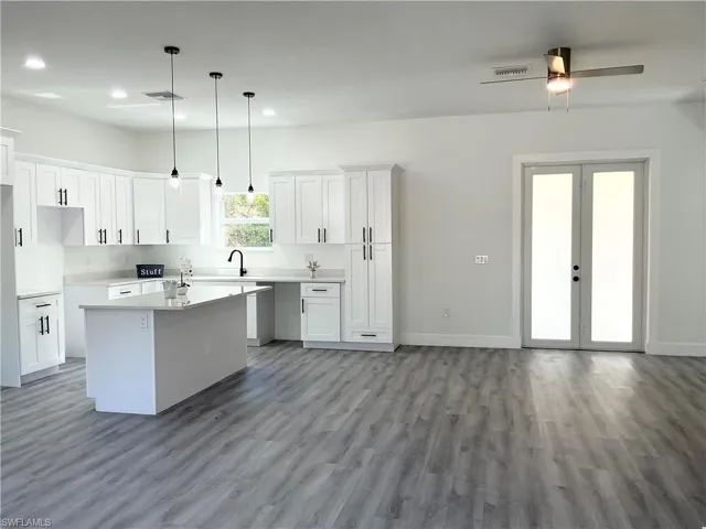 Kitchen with white cabinets, decorative light fixtures, a ceiling fan, a center island, and light wood finished floors
