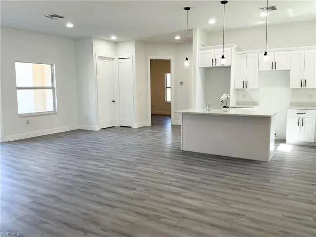 Kitchen with white cabinets, pendant lighting, open floor plan, a kitchen island with sink, and healthy amount of natural light