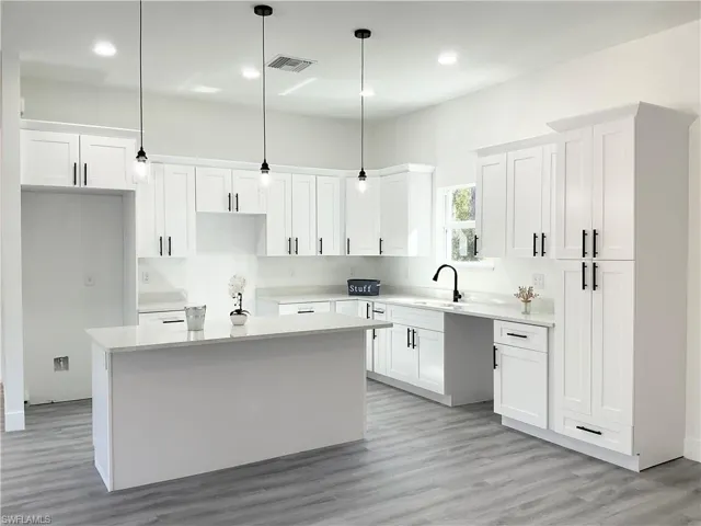Kitchen featuring white cabinetry, a center island, decorative light fixtures, light wood-style flooring, and light stone countertops