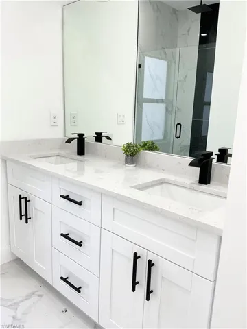 Bathroom featuring double vanity, light marble finish floors, and a marble finish shower