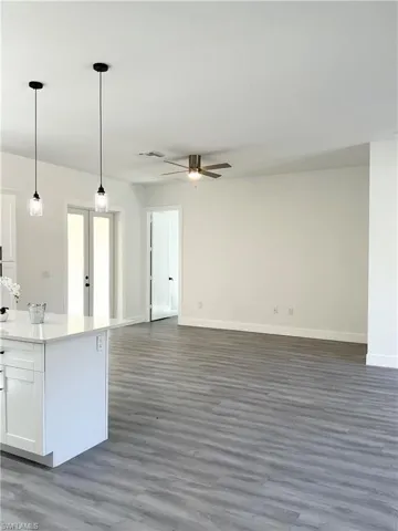 Kitchen with decorative light fixtures, open floor plan, light stone counters, white cabinetry, and dark wood-style floors