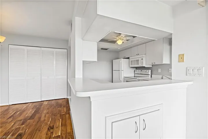 Kitchen featuring white appliances, kitchen peninsula, ceiling fan, dark wood-type flooring, and a tray ceiling