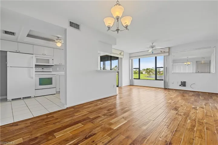 Kitchen with pendant lighting, light hardwood / wood-style floors, ceiling fan with notable chandelier, and white appliances