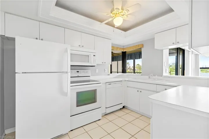 Kitchen with a tray ceiling, white appliances, and white cabinets