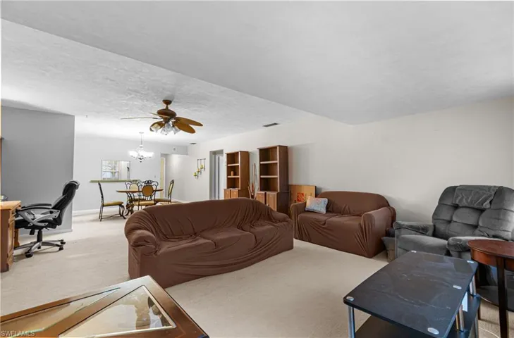 Living room with carpet flooring, a desk, ceiling fan, a textured ceiling, and a chandelier