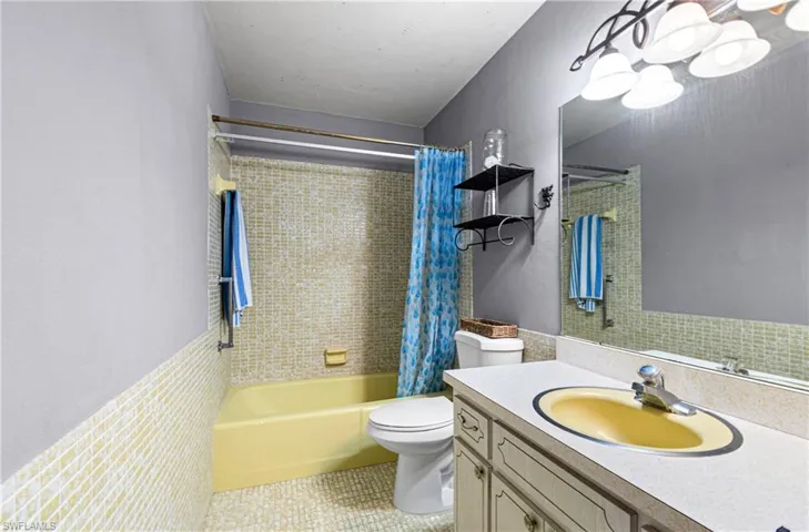 Full bathroom with shower / bath combo, vanity, light tile patterned floors, and wainscoting