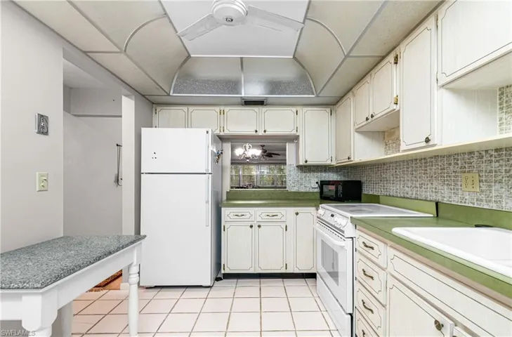 Kitchen featuring white appliances, light tile patterned floors, a ceiling fan, backsplash, and white cabinets
