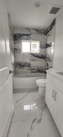 Full bathroom featuring vanity, marble finish flooring, and washtub / shower combination