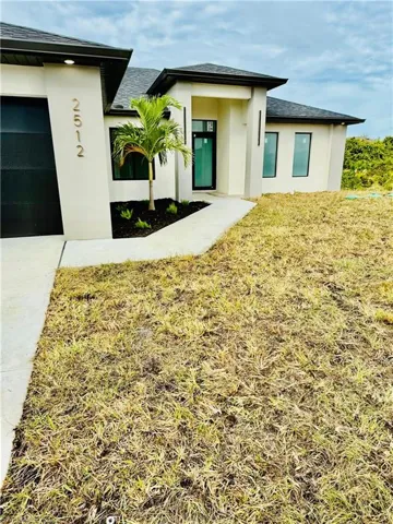 Entrance to property featuring roof with shingles, stucco siding, a lawn, and an attached garage