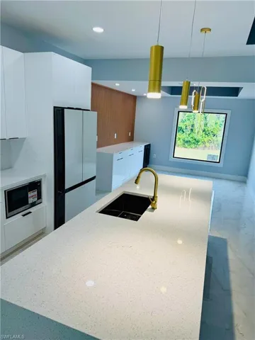 Kitchen featuring white cabinets, modern cabinets, light stone counters, freestanding refrigerator, and hanging light fixtures