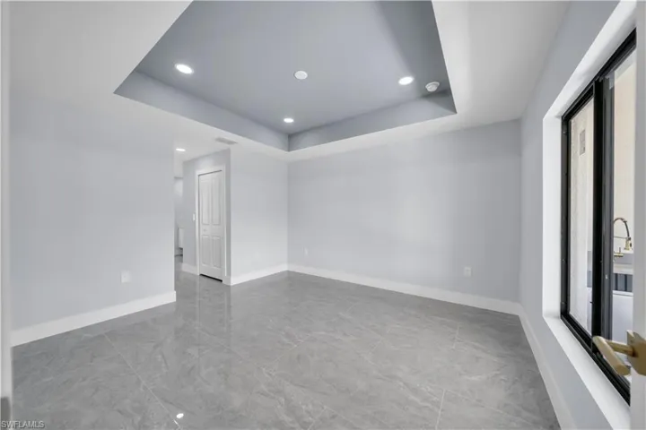 Spare room featuring a raised ceiling, recessed lighting, and light marble finish flooring