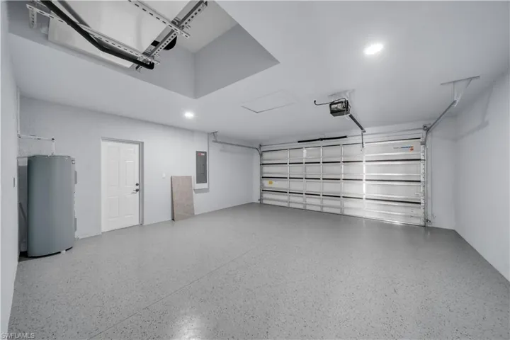 Garage featuring water heater, electric panel, recessed lighting, and a garage door opener
