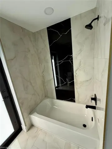 Bathroom with marble finish floors and bathing tub / shower combination