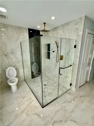 Bathroom with marble tiled floors, stone wall, a marble finish shower, tile walls, and recessed lighting