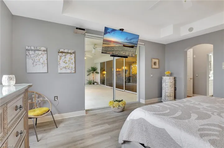 Bedroom featuring light wood-style floors, a raised ceiling, arched walkways, a ceiling fan, and multiple windows