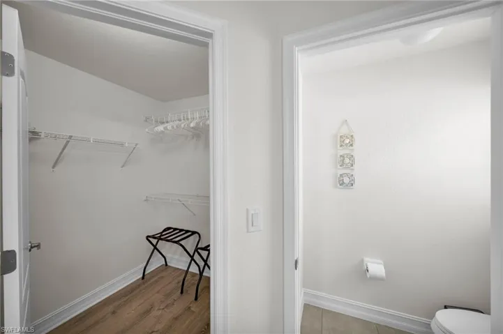 Bathroom with toilet, a spacious closet, wood finished floors, and baseboards