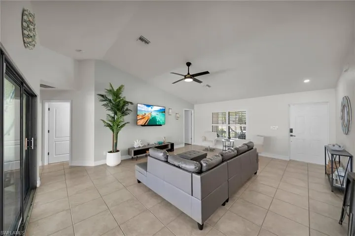 Living area with visible vents, ceiling fan, light tile patterned flooring, and lofted ceiling